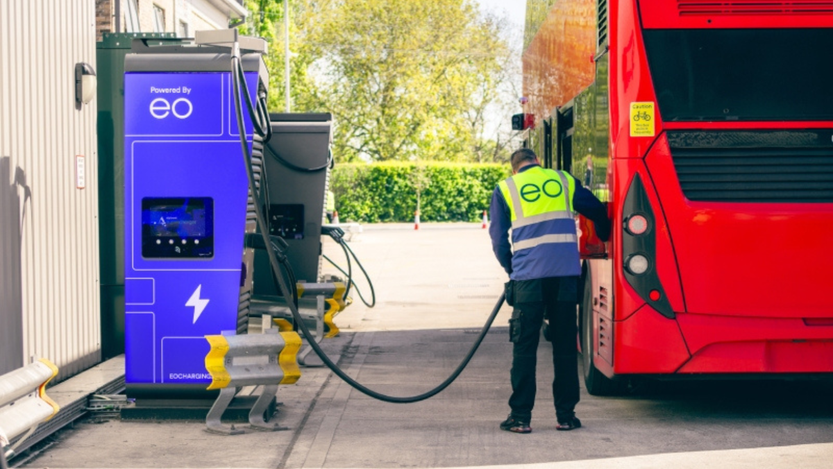 Worker charging an electric bus using EO Charging equipment beside bright blue charger unit