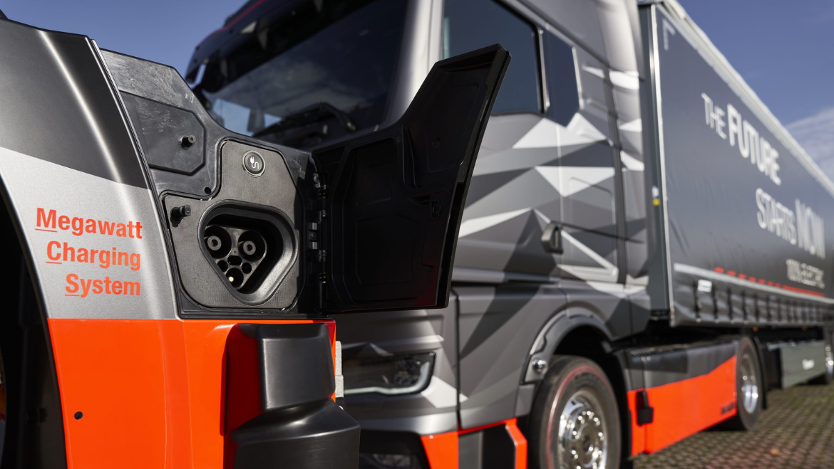 Close-up of megawatt charging port on electric truck with heavy-duty vehicle in background.