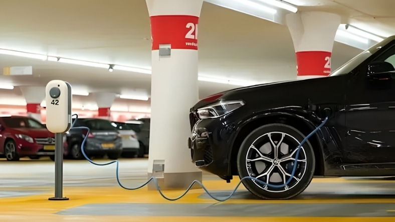Black electric car plugged into charging station indoors